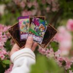 A hand holding Yu-Gi-Oh! cards with vibrant floral background, perfect for collectors and enthusiasts.