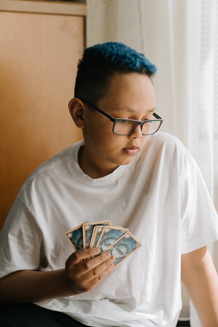 A boy in a white t-shirt and glasses focuses on strategy card game indoors.